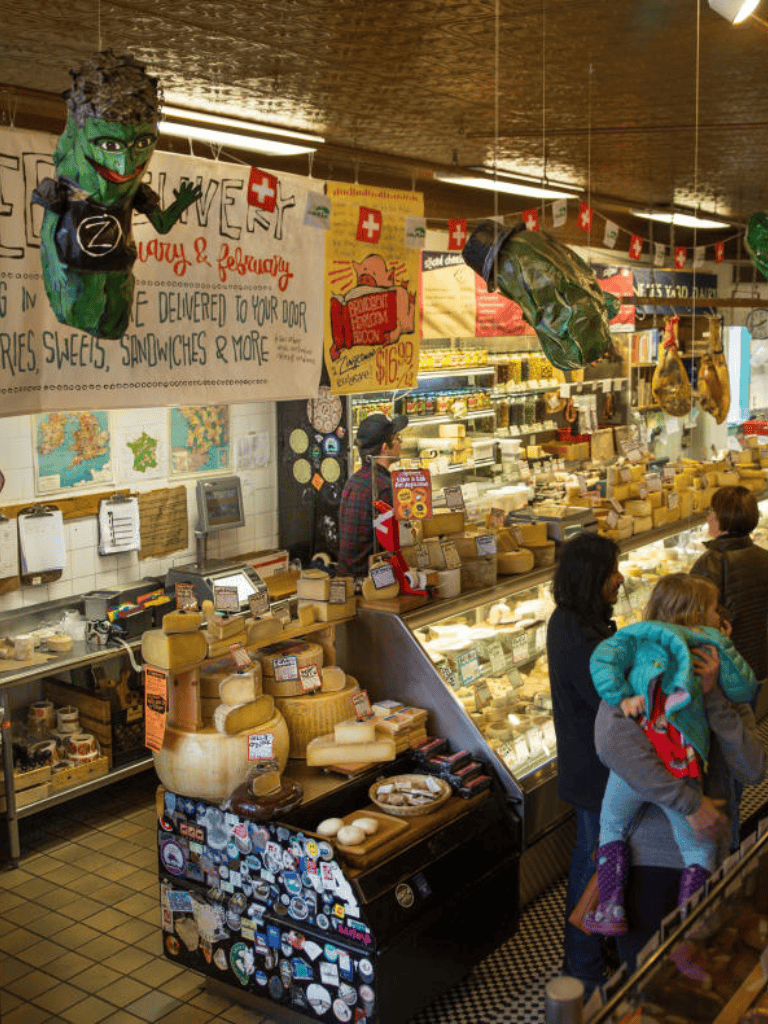 Aisle of Swiss cheese at a cheese shop with customers shopping and colorful decorations.