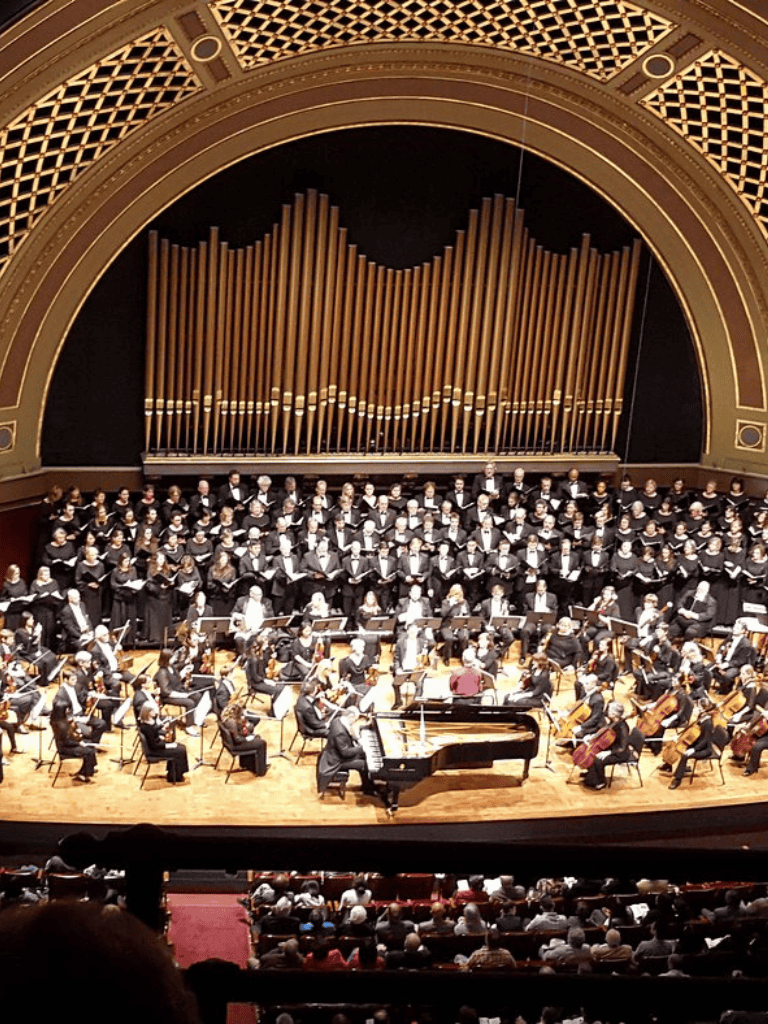 Elegant orchestra performing on stage at a concert hall with a grand pipe organ backdrop.