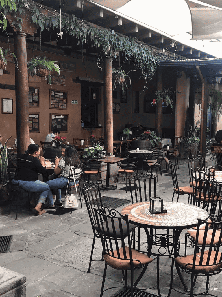 Cozy outdoor cafe with wooden decor, green plants, and seating for socializing and dining.