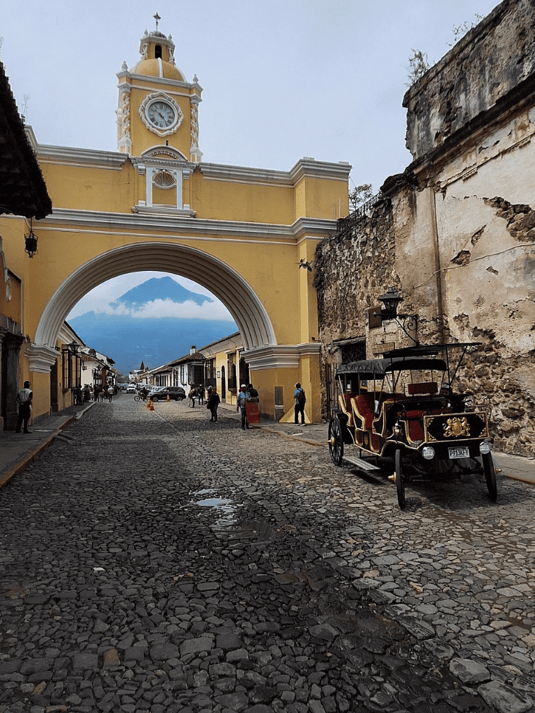 Historic street scene in Antigua Guatemala with colonial architecture and a horse-drawn carriage.