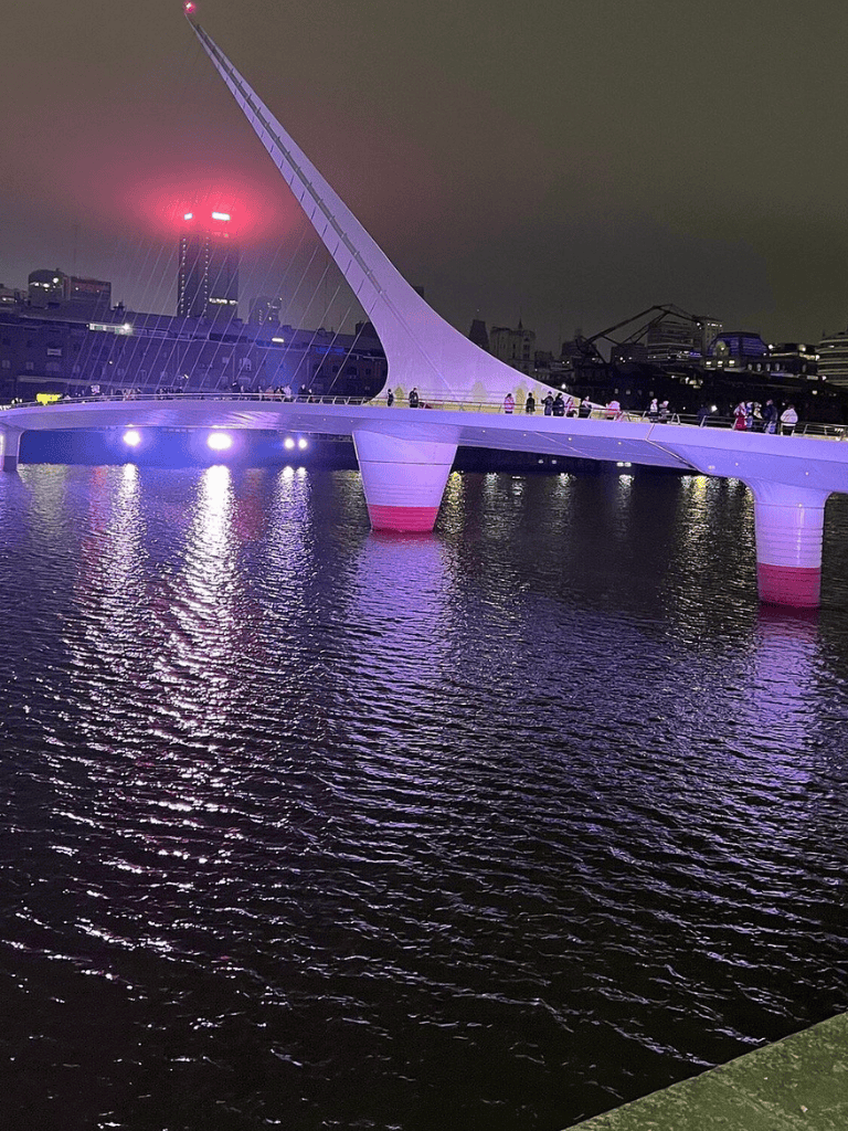 Colorful illuminated pedestrian bridge at night in Dublin, Ireland, with city skyline reflections.
