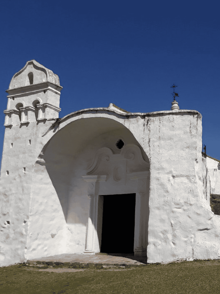 Historic white mission church with bell tower in Mexico under clear blue sky.