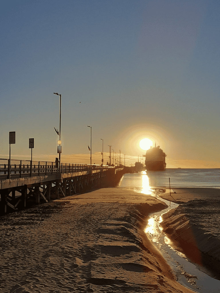 Sunset at the beach with pier and ship, perfect for travel and coastal adventure keywords.