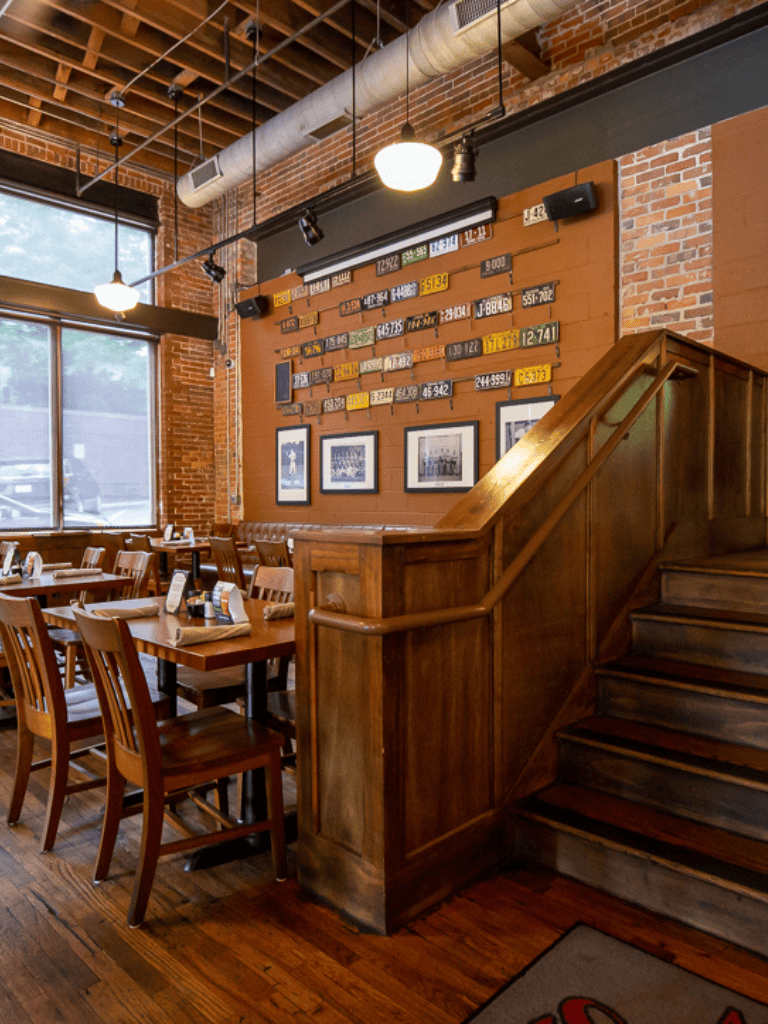 Cozy restaurant interior with brick walls, wooden furniture, and decor featuring vintage license plates, perfect for dining and social gatherings.