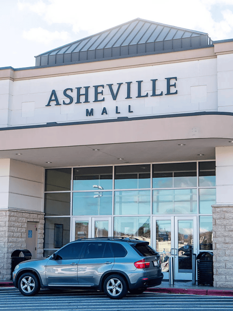 Bright daylight outside Asheville Mall with a parked silver SUV in front of the entrance.