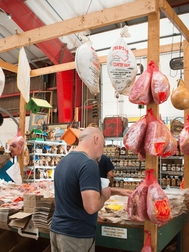 Smoked ham hanging at a local market for sale, showcasing fresh meat products.