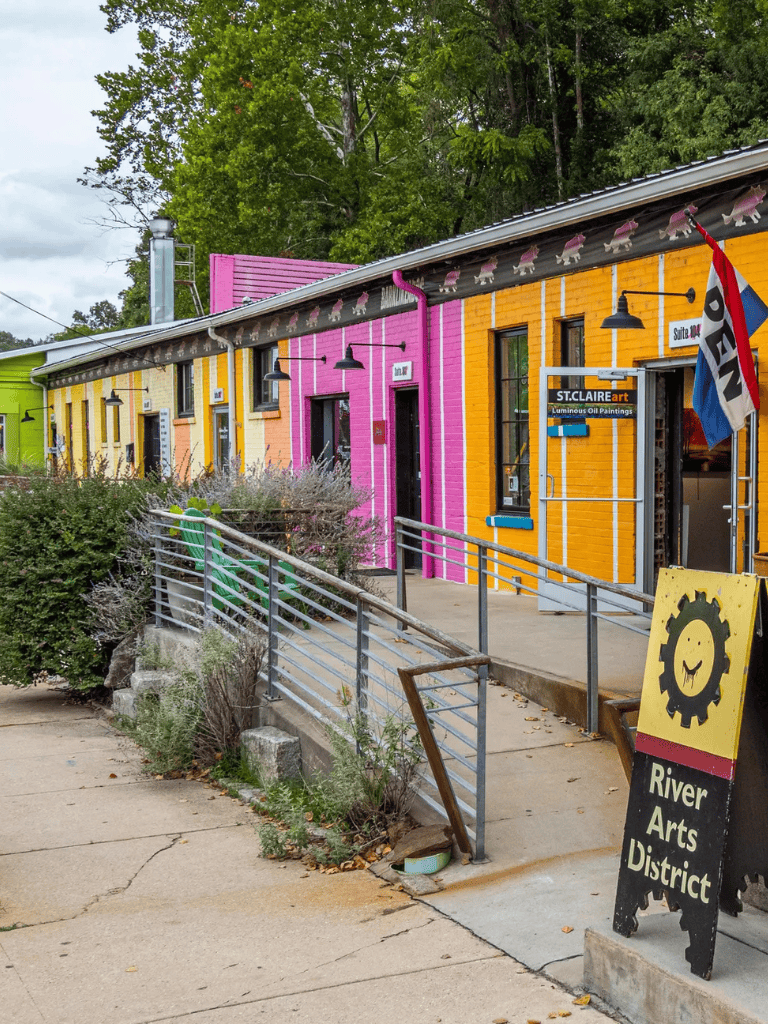 Colorful arts district storefronts with vibrant yellow and pink buildings, outdoor signage, and a ramp entrance in a lively district.