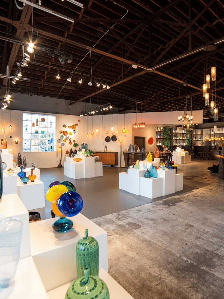Colorful glass art pieces displayed in an art gallery with warm lighting and industrial ceiling.