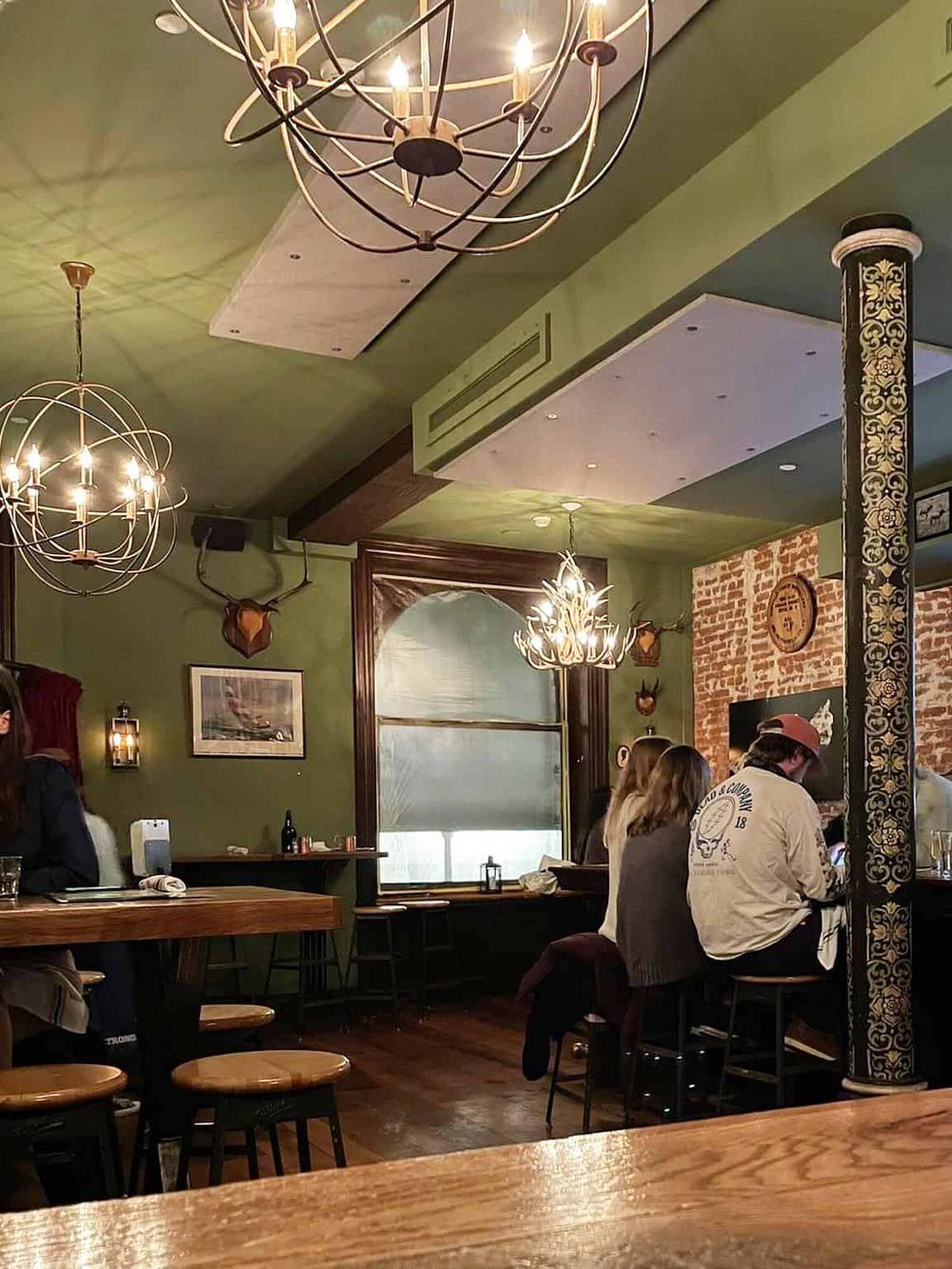 Cozy pub interior with rustic decor, chandeliers, and brick wall, perfect for social dining and relaxation.