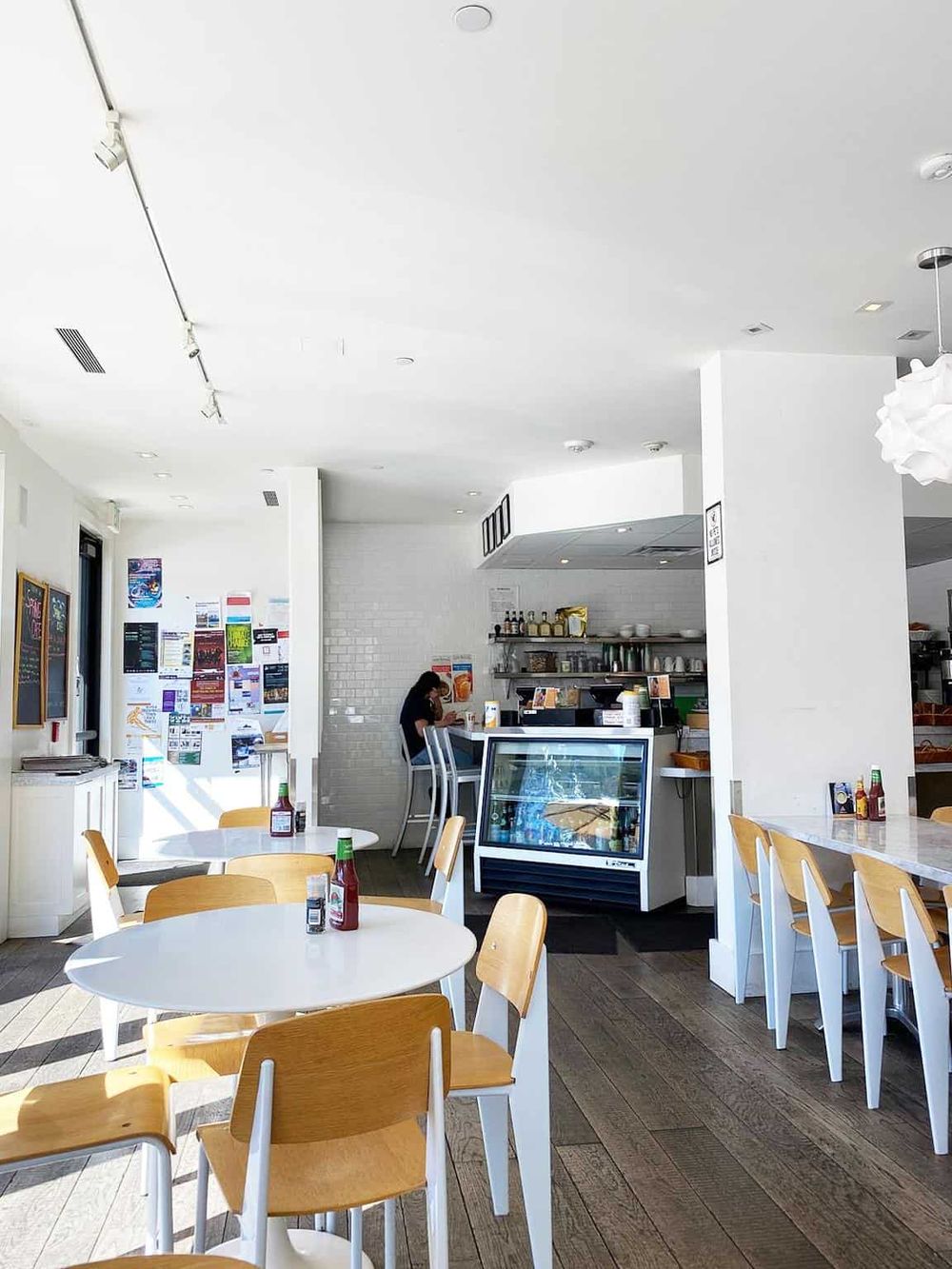 Cozy cafe interior with white tables, wooden chairs, and a minimalist design, perfect for relaxed dining experiences.