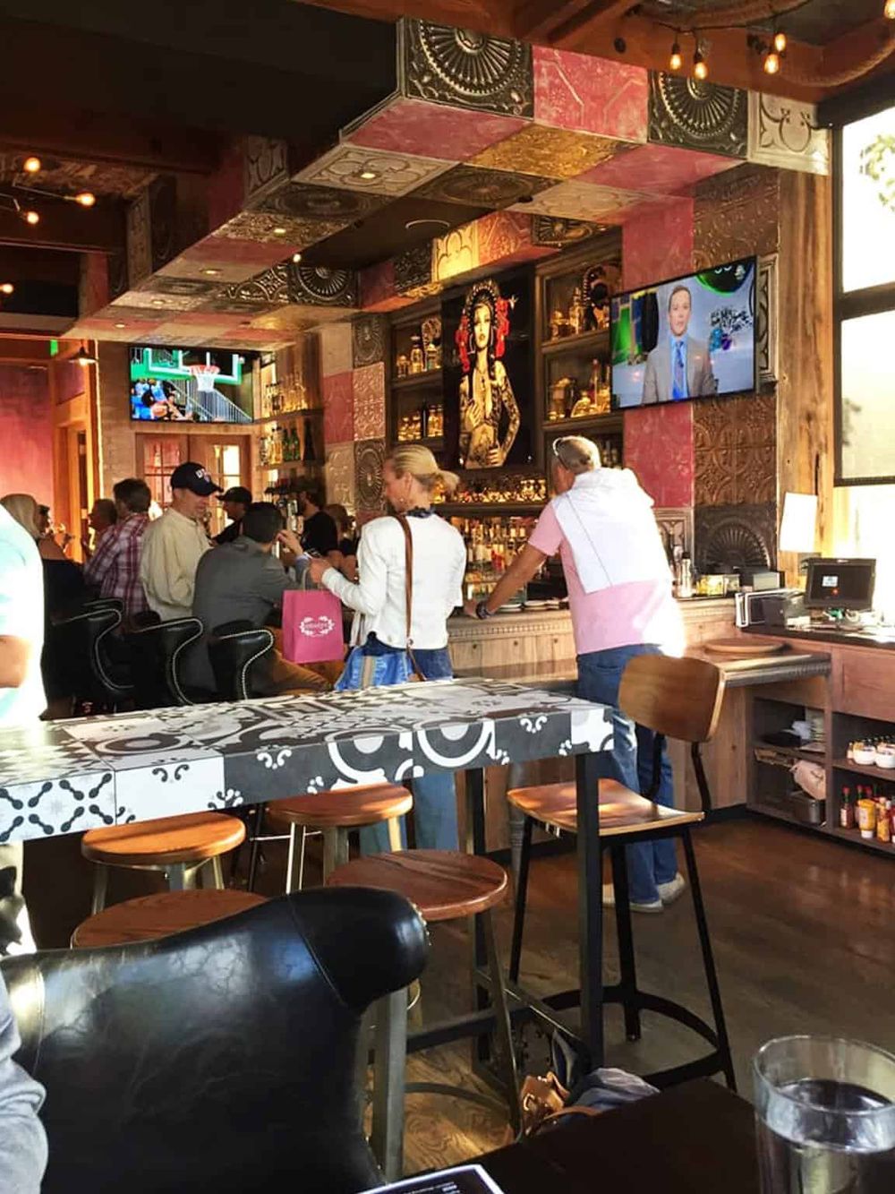 Vibrant bar interior with eclectic decor, diverse patrons, and large screens showcasing sports and entertainment.