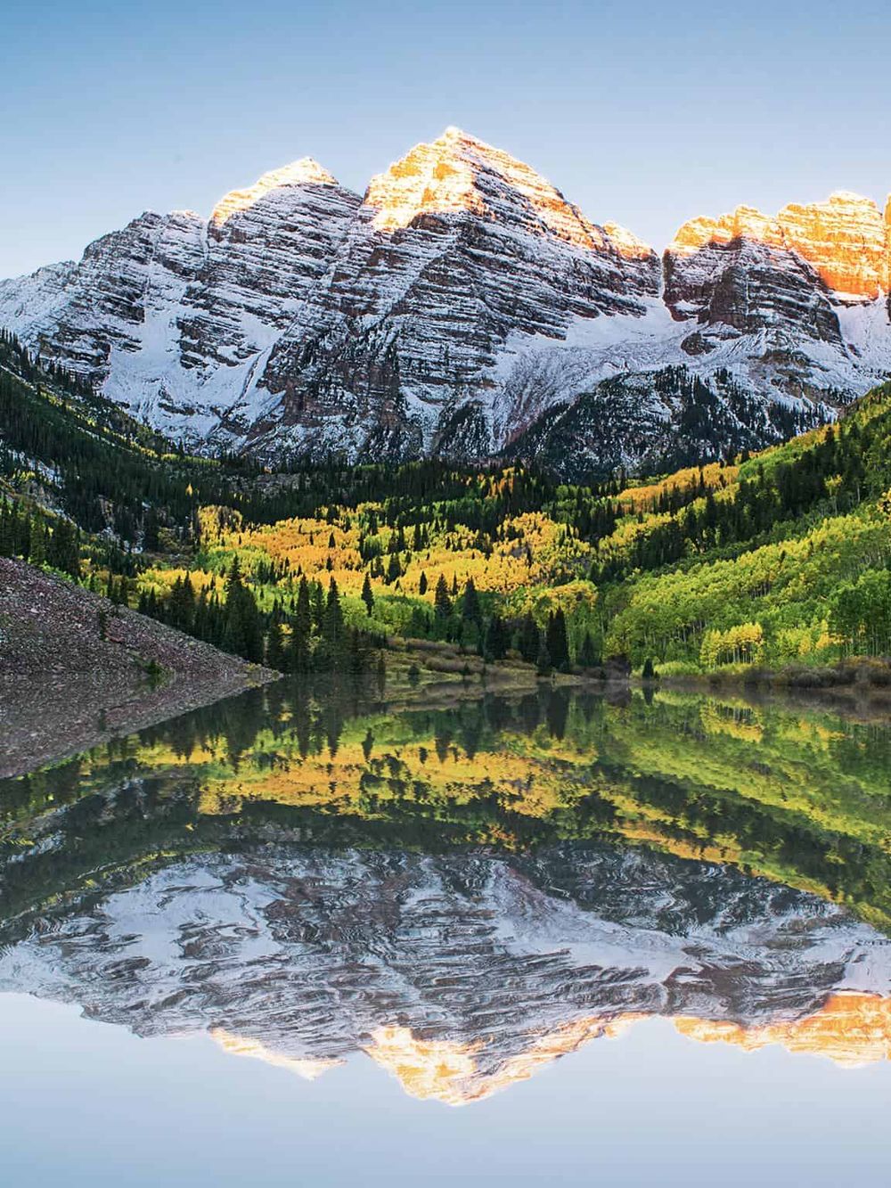 Snow-capped mountain range with lush green forest and calm lake reflection in the Rockies.