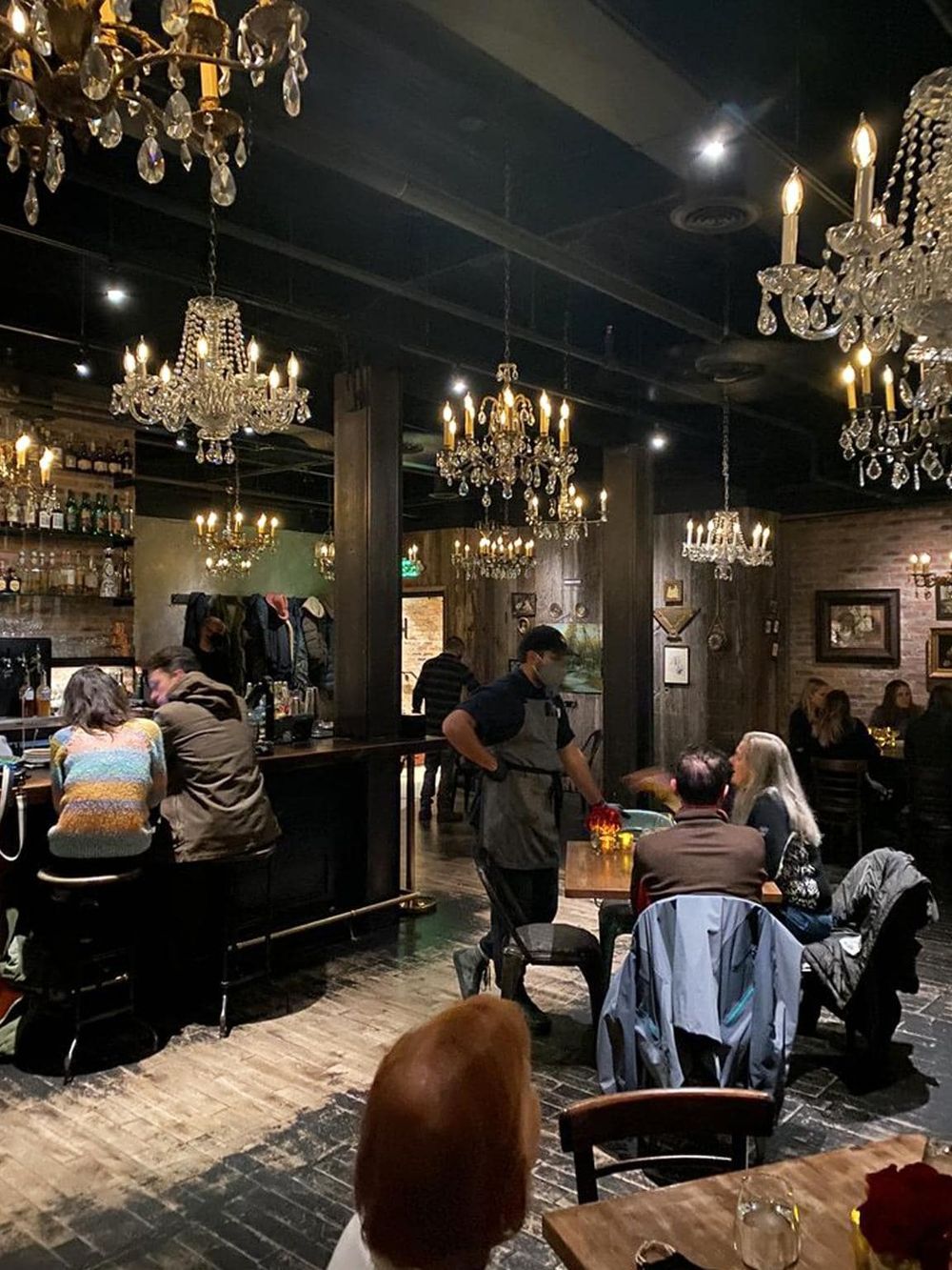 Cozy restaurant interior with chandelier lighting, modern rustic decor, and diners enjoying meals and drinks.