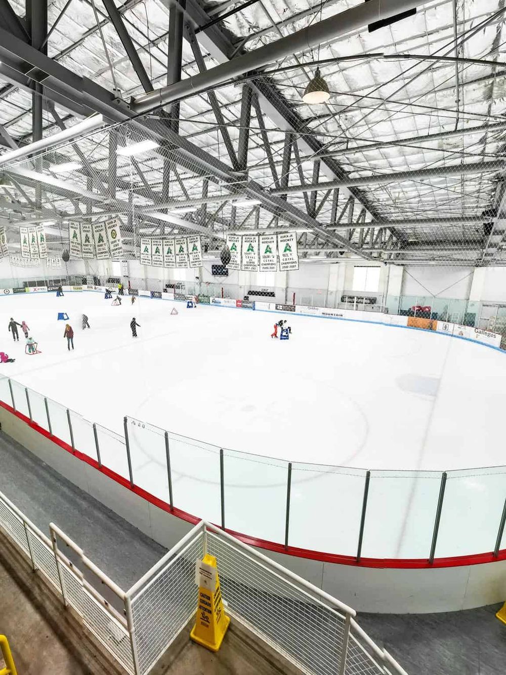 Bright indoor ice hockey rink with players skating and practicing. Modern arena with banners and industrial ceiling.