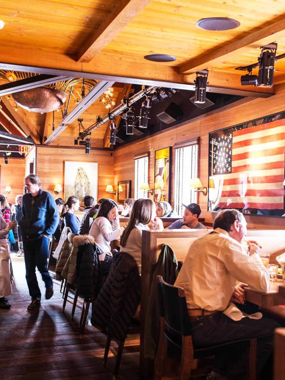 Cozy restaurant interior with wooden decor, American flag art, and diners enjoying their meals, perfect for American cuisine dining experience.