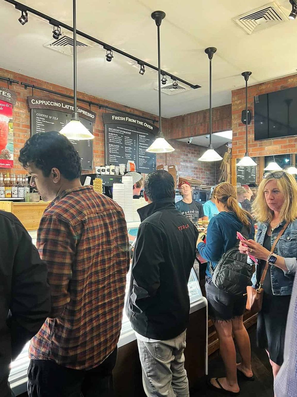 People ordering food at a bustling cafe counter, modern brick interior, showcasing quick-service dining experience.