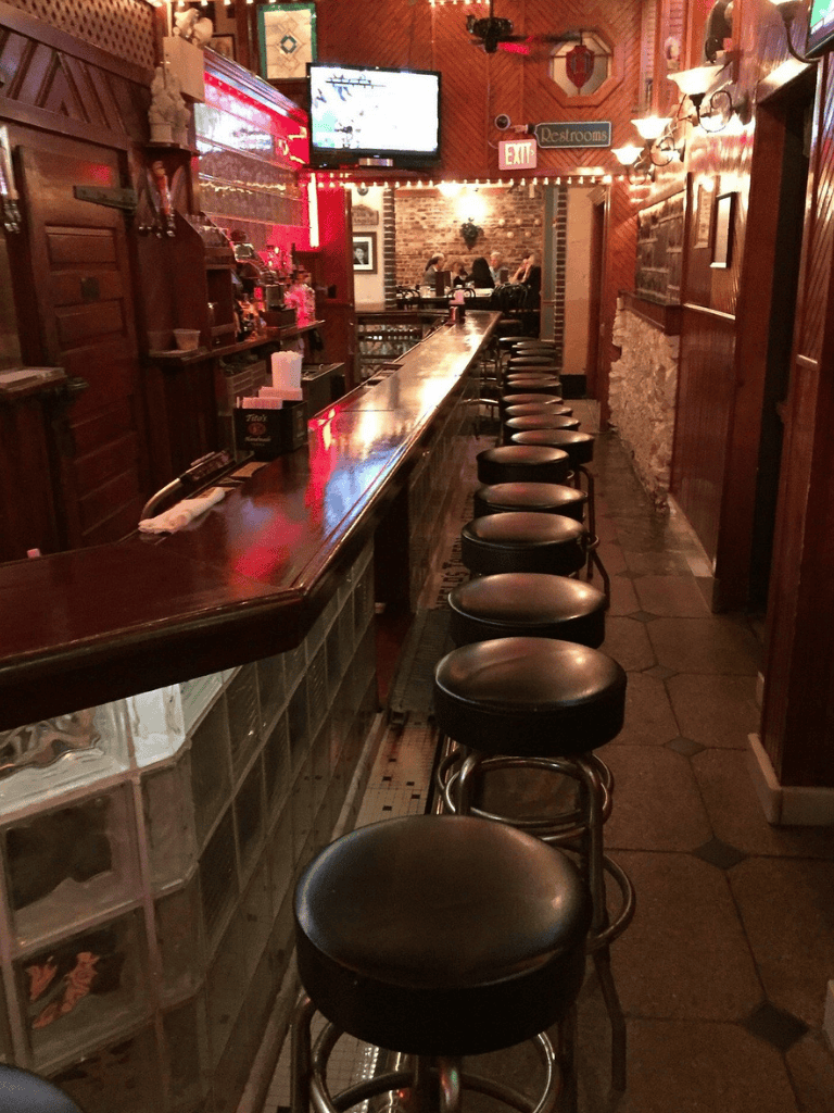 Cozy bar interior with a long wooden counter and black stools in a warm, inviting atmosphere.