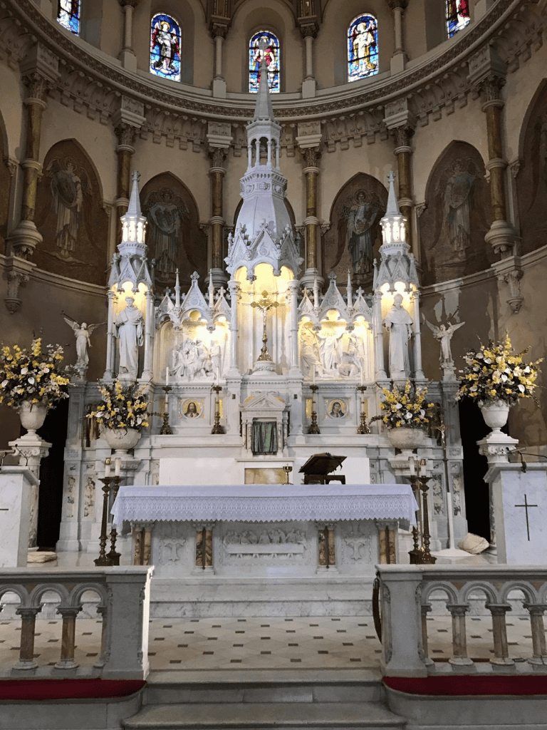 Elegant church altar with ornate marble, statues, and stained glass windows.