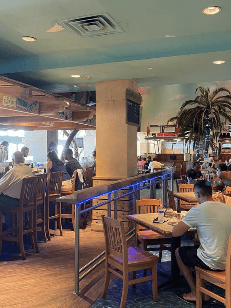 Indoor restaurant scene with diverse patrons dining and socializing, featuring tropical decor and casual ambiance.
