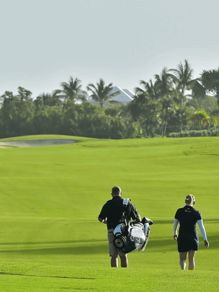 1. Golf course with two players carrying golf bags and palm trees in the background.
