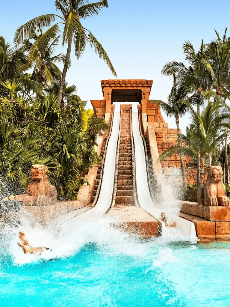 Thrilling water slide at tropical resort with lush greenery and ancient stone statues.