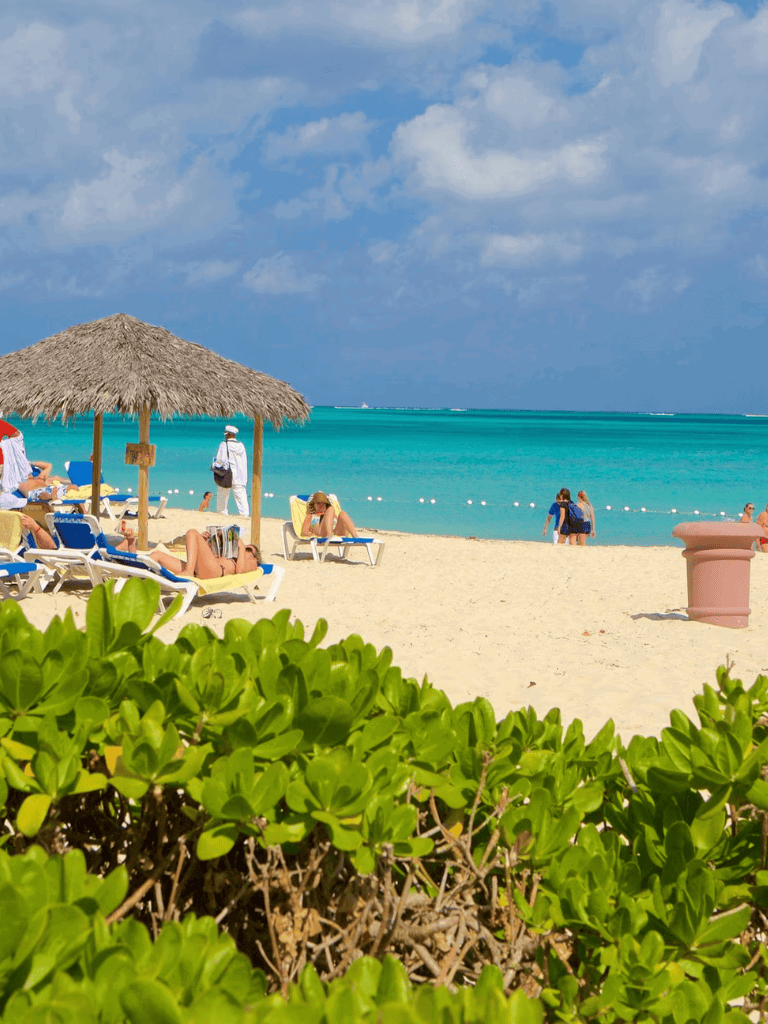 Tropical beach with lounge chairs, umbrellas, and turquoise waters, sunny day.