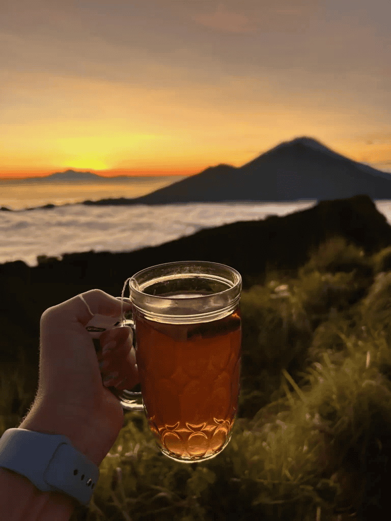 A serene sunrise over a mountain with a hand holding a glass of tea, capturing tranquility and natural beauty.