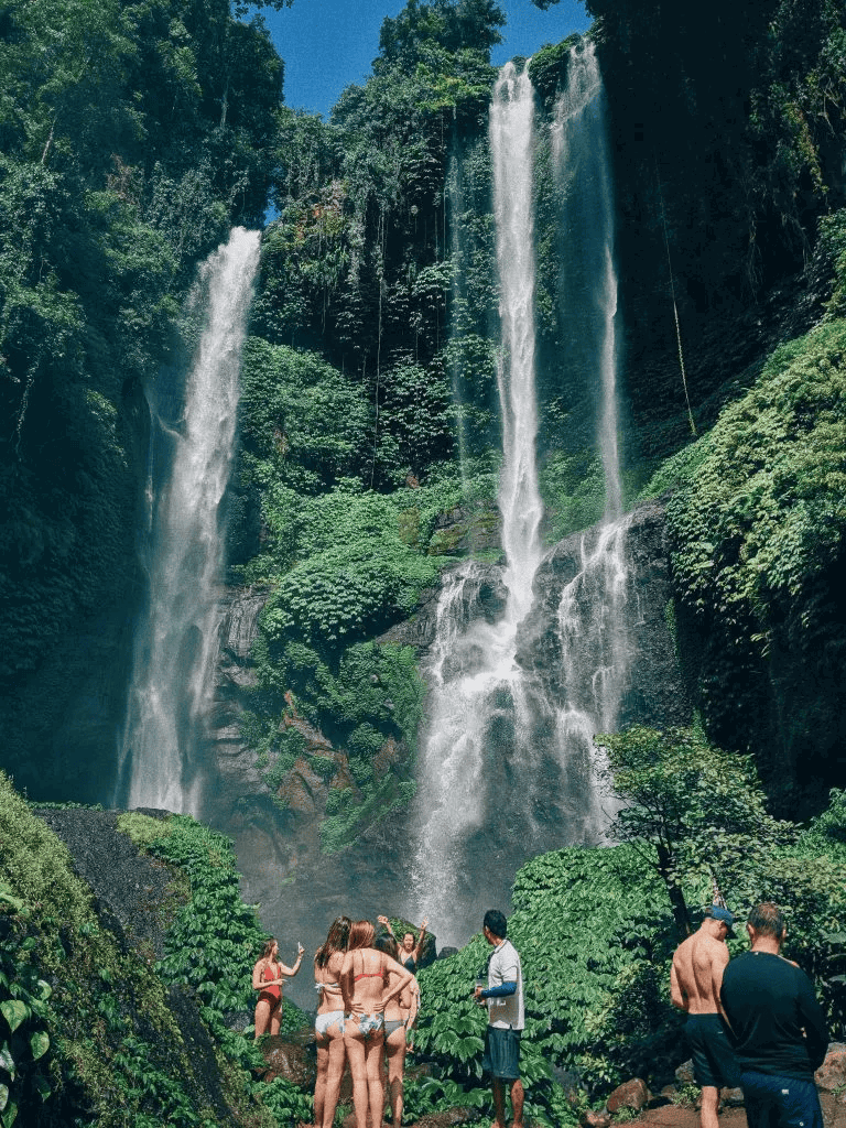 Vibrant jungle waterfall with tourists enjoying the scenic view and lush greenery surrounding the cascading water.