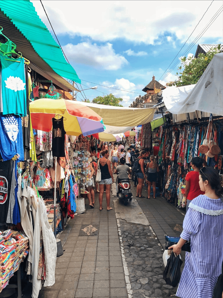 Colorful outdoor market in Bali with clothing, accessories, and souvenirs under vibrant umbrellas.
