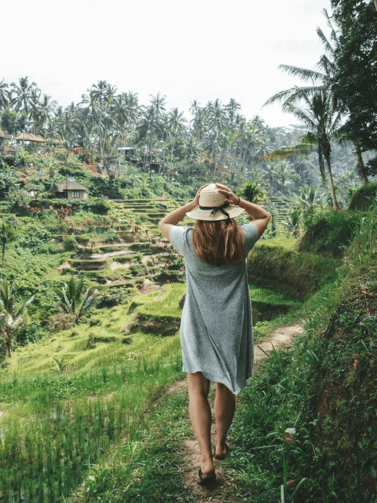 Lush green terraced rice fields with a woman walking on a dirt path, tropical landscape, eco-tourism, adventure travel.
