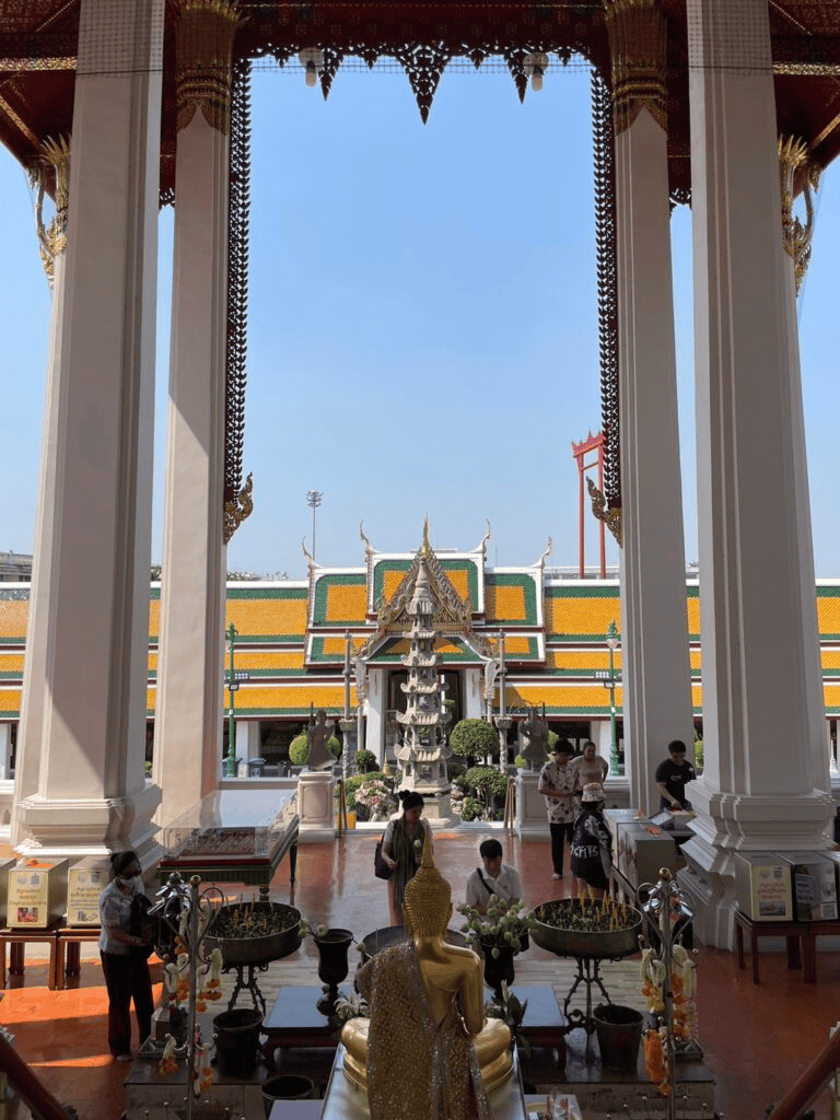 Intricate Thai temple interior with Buddha statue, worshippers, and traditional architecture.