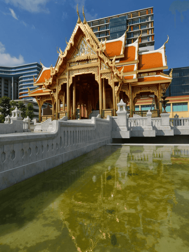 Traditional Thai temple with modern city buildings in the background, showcasing cultural architecture and urban landscape.