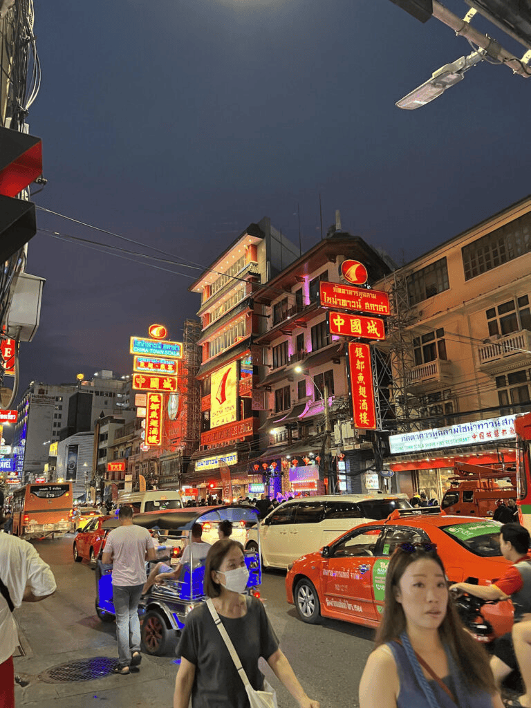 Bright nightlife scene in Bangkok with colorful neon signs and busy streets filled with cars and pedestrians, showcasing vibrant city life.