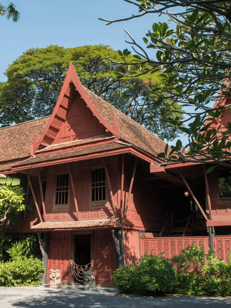 Traditional Thai wooden house with intricate design and lush greenery in the background.