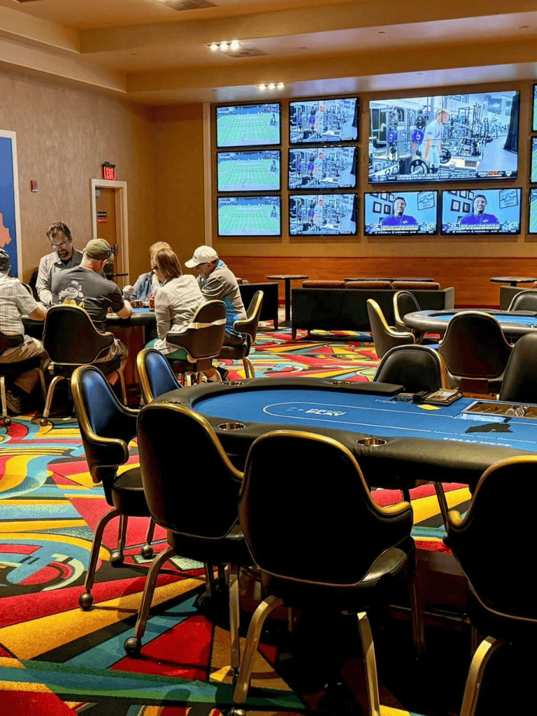 Luxurious casino poker game room with multiple tables and large screens for sports betting and entertainment.