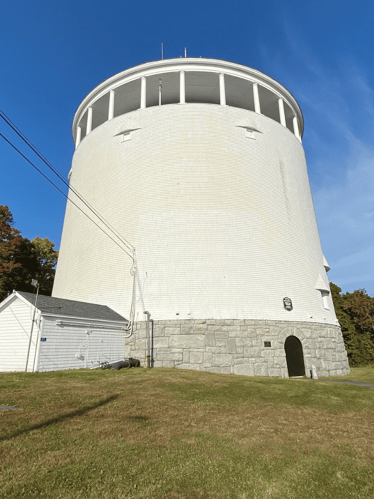 White historic lighthouse tower with stone base against blue sky, coastal navigation aid.