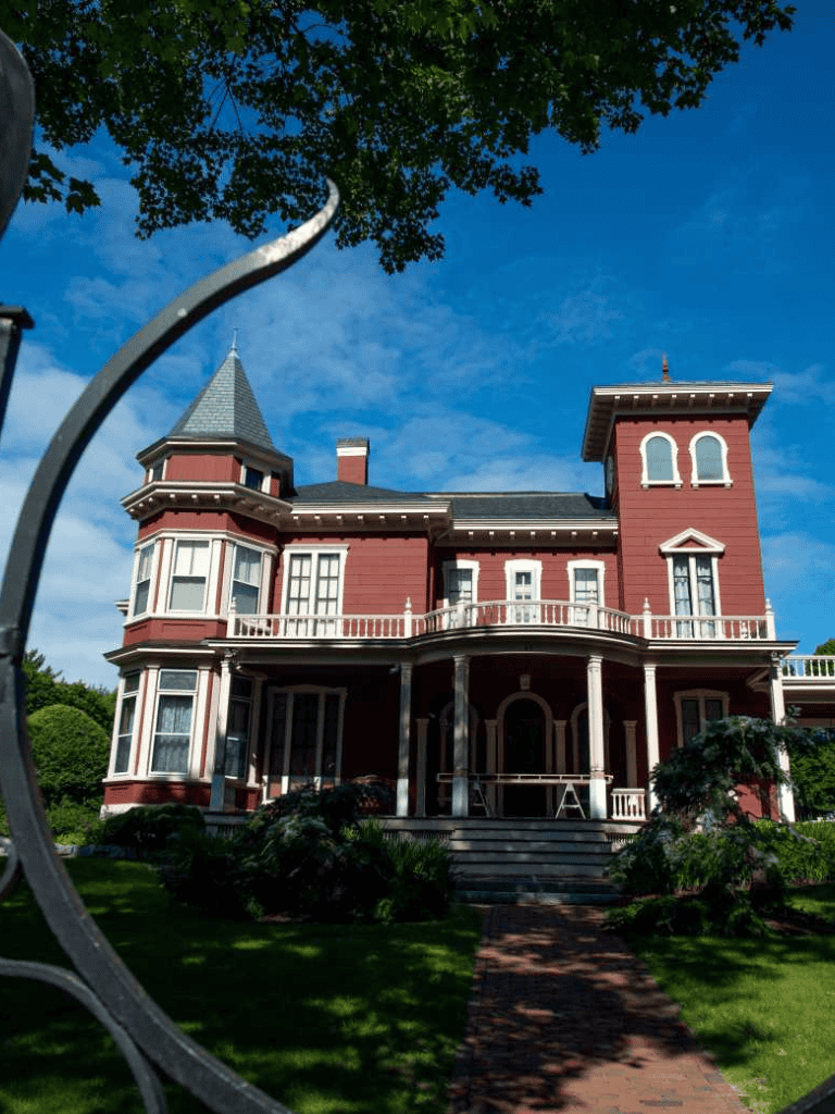 Victorian mansion on a lush green lawn with a clear blue sky background.