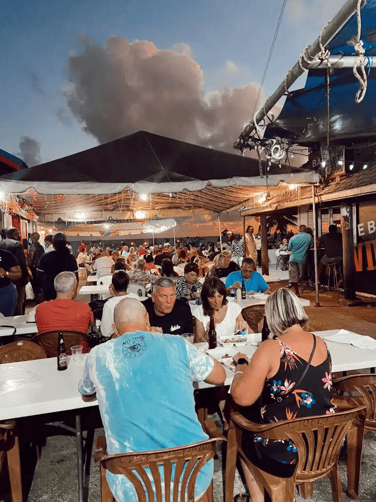 Outdoor restaurant at sunset with people dining and enjoying the seaside view.