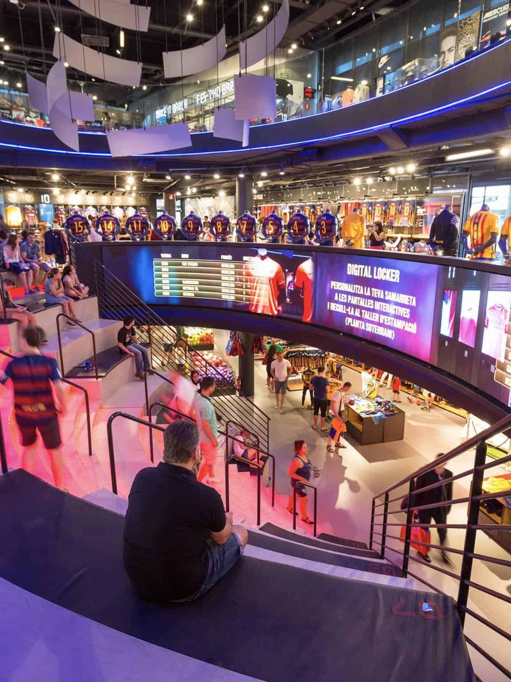 Vibrant modern shopping mall interior with digital signage, visitors, and sports merchandise displays.