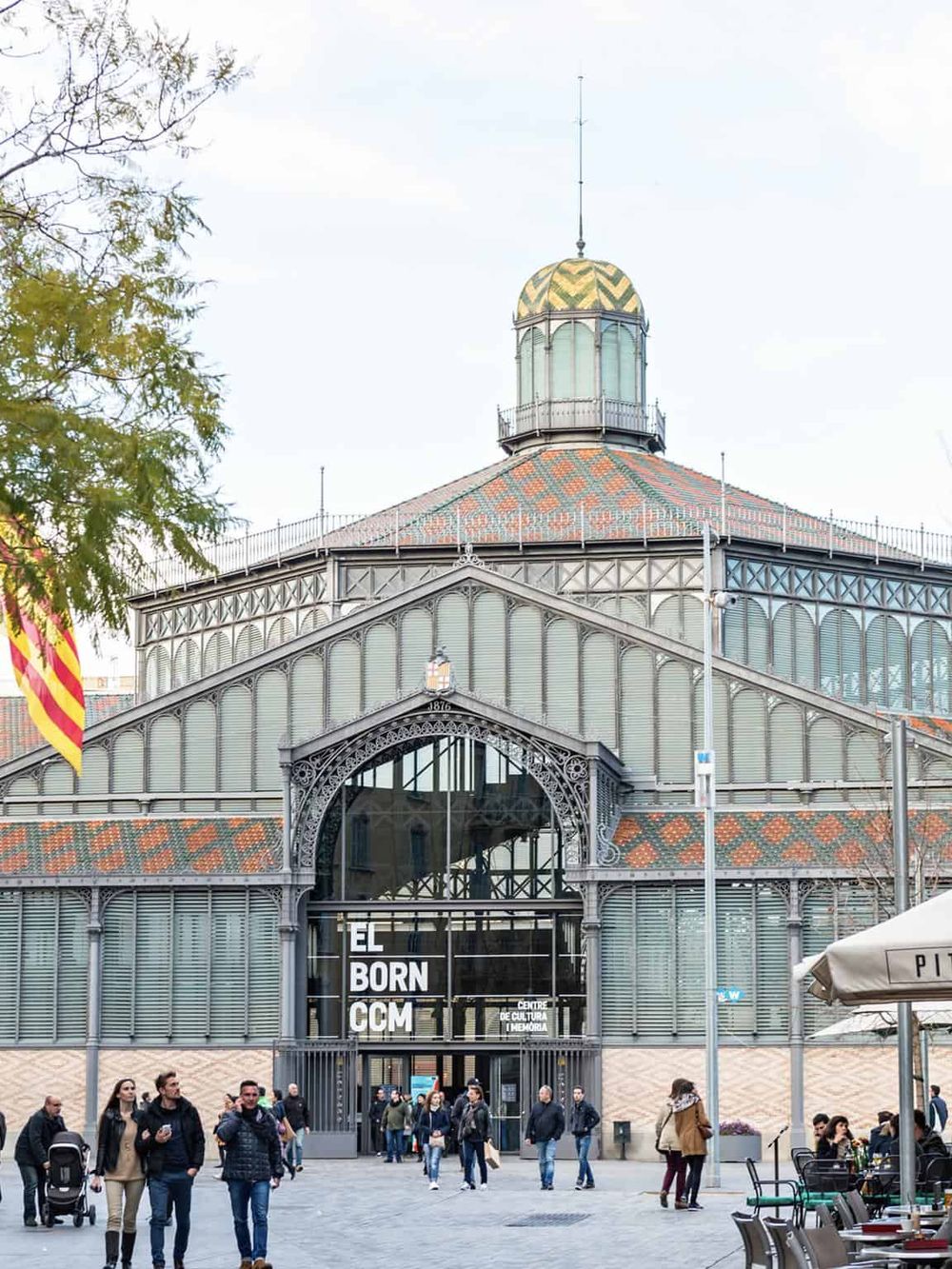 Colorful historic glass greenhouse in Barcelona with visitors and cultural center signage.