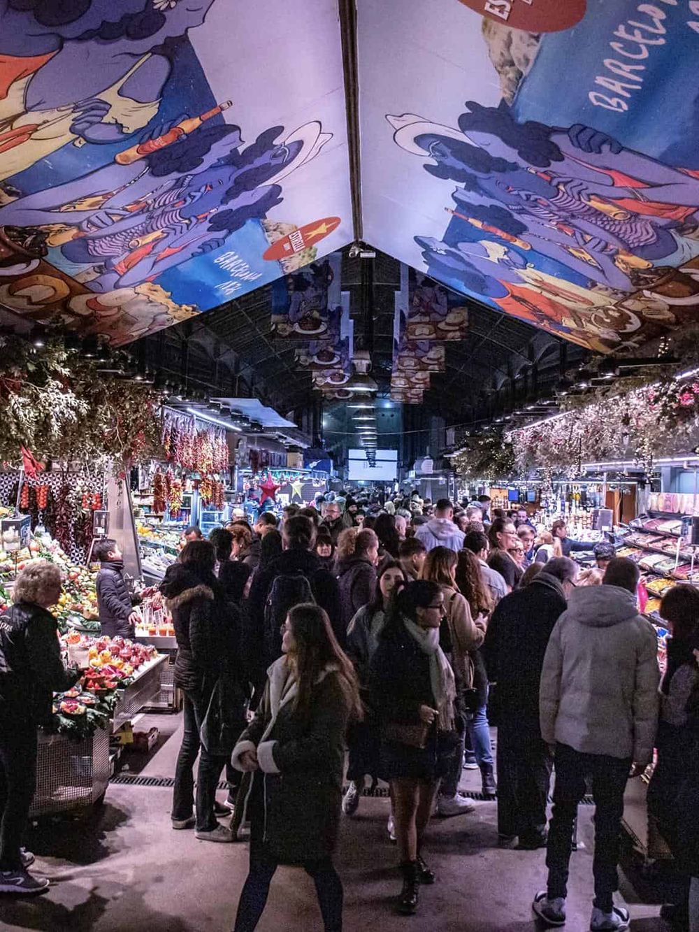 Colorful indoor market crowded with shoppers, vibrant displays, festive decorations, and overhead murals.