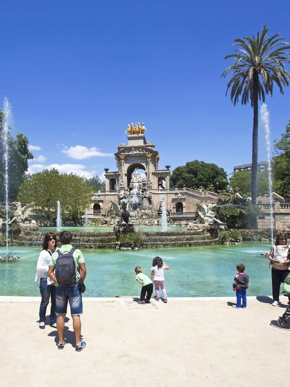 Colorful park fountain with visitors under blue sky, ideal for family travel and sightseeing.