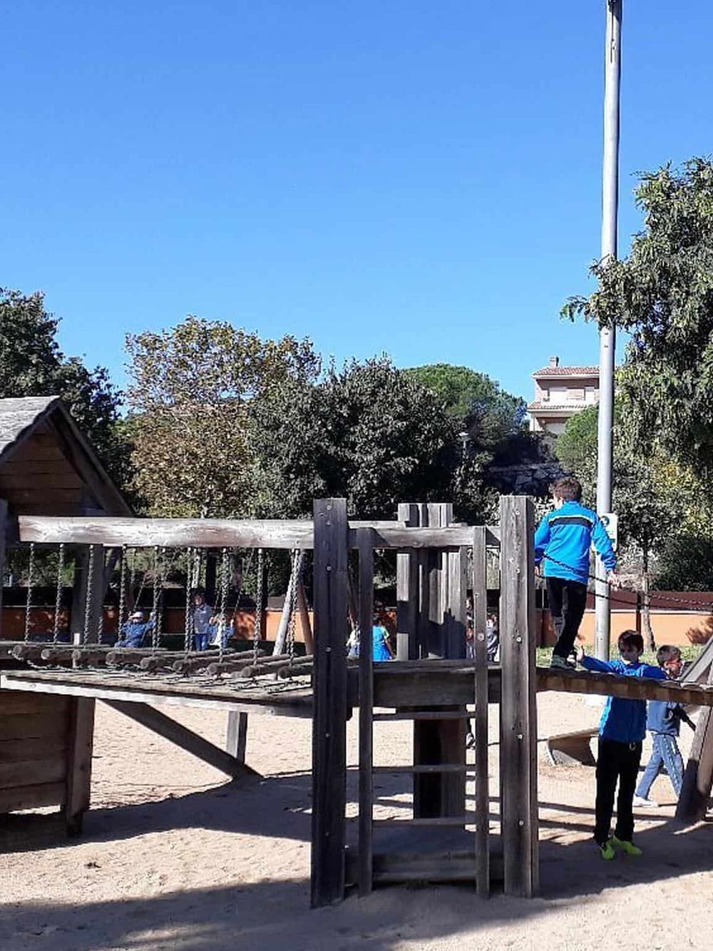 Children playing on wooden playground equipment at a park, family-friendly outdoor activity, sunny day, kids having fun.