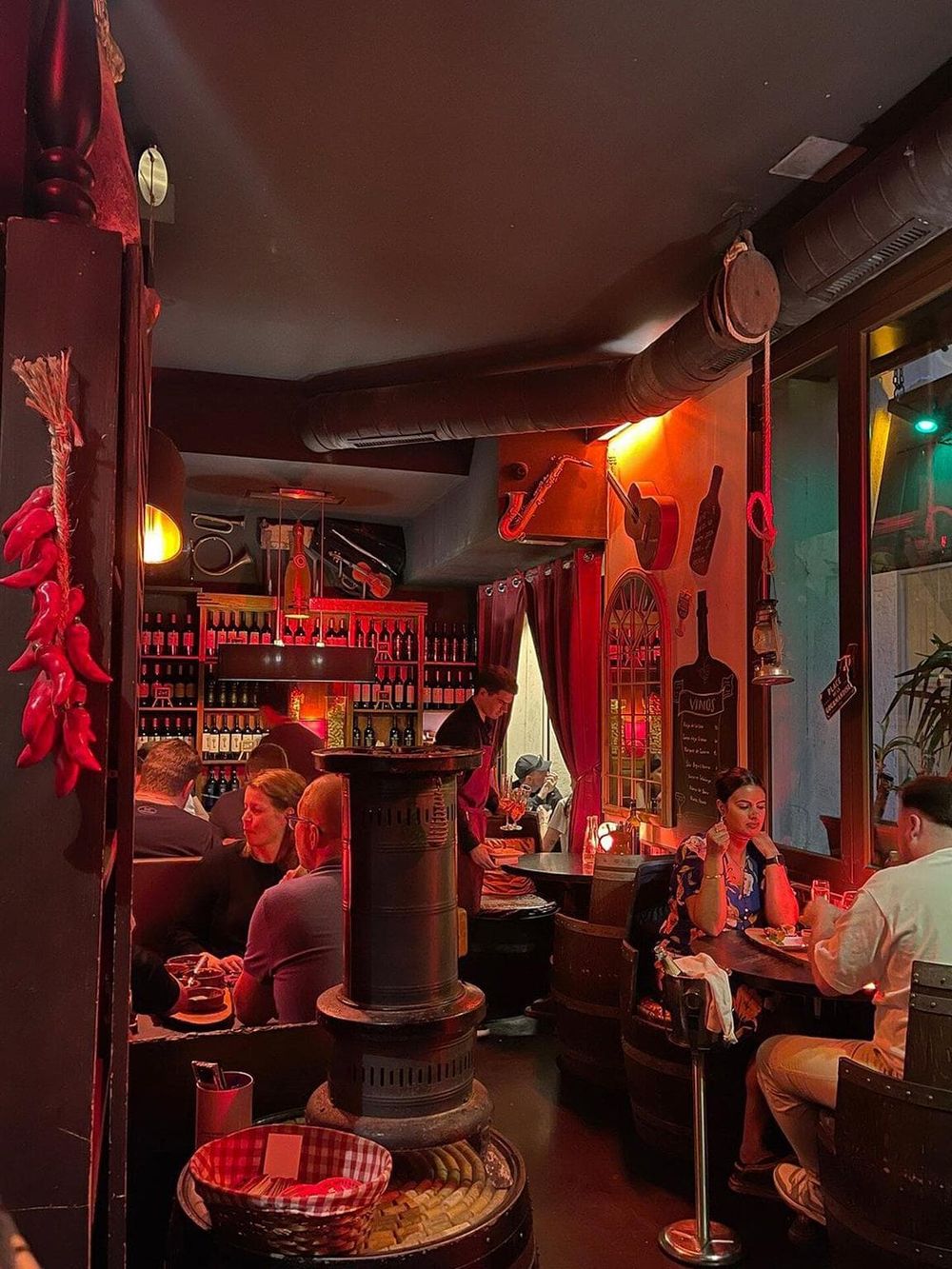 Cozy restaurant interior with warm red lighting, wine bottles display, and lively dining atmosphere.