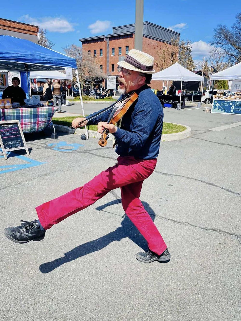 Vibrant street performer playing violin at outdoor market, lively atmosphere, community event, live music, local vendors, entertainment.