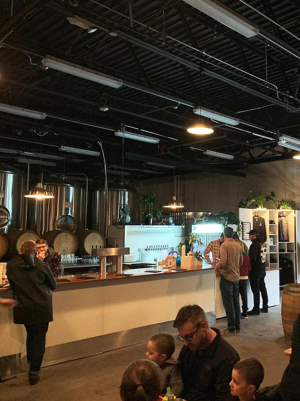Modern brewery interior with people socializing and beer tanks in the background.