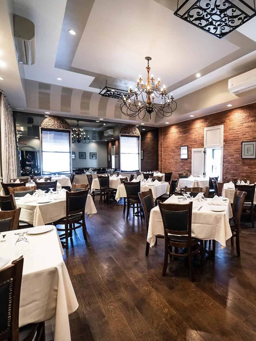 Elegant restaurant interior with brick walls, chandeliers, and neatly arranged white tablecloths.