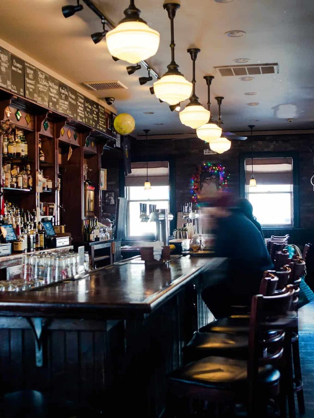 Cozy bar interior with warm lighting, festive decorations, and a customer enjoying a drink at the counter. Perfect for a relaxed dining experience.