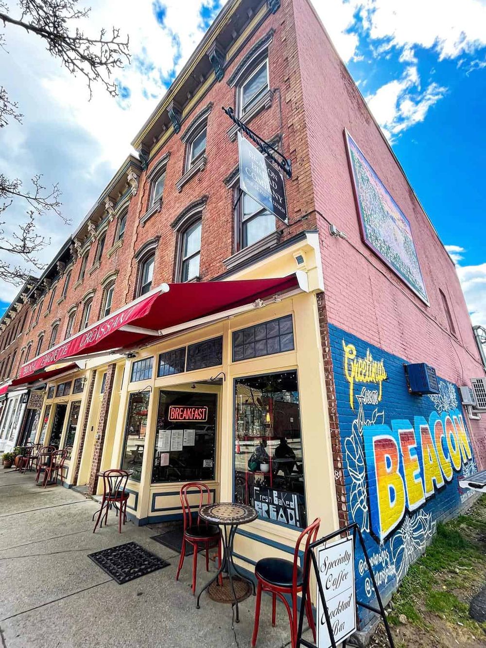 Colorful cafe on a corner with outdoor seating and vibrant mural, in a historic brick building.