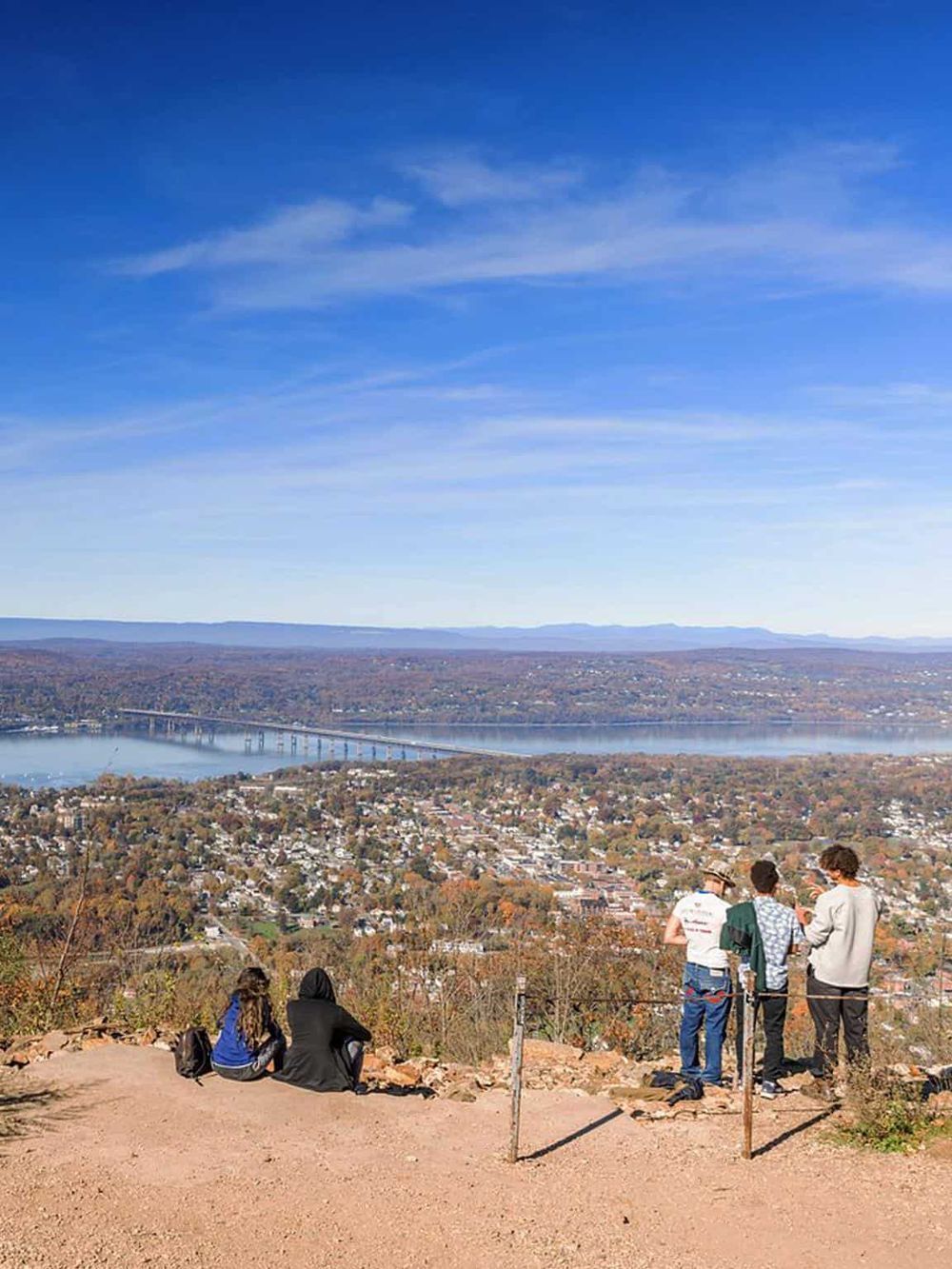 Breathtaking view from a popular hiking spot showcasing a city, river, and bridge under a bright blue sky.